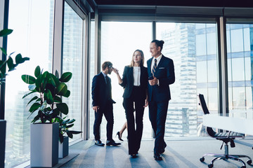 Young confident male and female employees walking in office together having friendly conversation on break, administrative assistant showing male colleague working space discussing cooperation