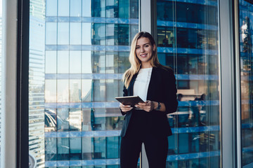 Half length portrait of Caucasian female entrepreneur with modern touch pad in hands smiling at camera posing in office interior, prosperous business woman in elegant suit holding digital tablet - obrazy, fototapety, plakaty