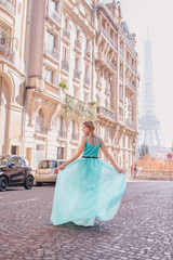 Obraz premium Beautiful young girl in a dress on the street with a view of the Eiffel tower