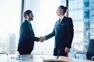 Cheerful male colleagues in formal elegant suit satisfied with getting agreement on business cooperation after meeting in office,men managers gesturing shaking hands having friendly conversation