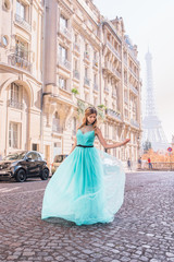 Fototapeta premium Beautiful young girl in a dress on the street with a view of the Eiffel tower