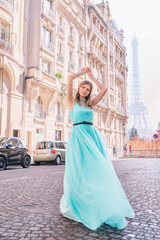 Fototapeta na wymiar Beautiful young girl in a dress on the street with a view of the Eiffel tower