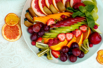 a plate of fruit assorted. Kiwi, grapefruit, oranges, apples, grapes and strawberries. On a white plate. Healthy food