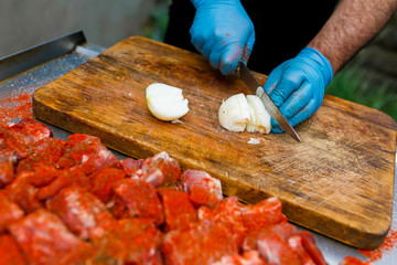 Close-up. A male cook cuts onions on a wooden board for a prepared kebab of red meat.