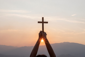 human praying to the GOD while holding a crucifix symbol with bright sunbeam on the sky