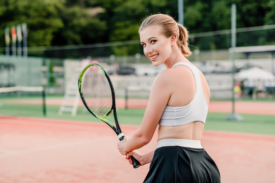 smiling tennis player looking over shoulder on court with racket