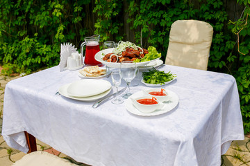Beautifully served table with barbecue sauce and glasses for wine on a background of green hedges
