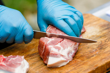 Close-up. A cook man in blue disposable gloves cuts a piece of red meat into pieces.