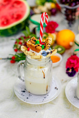 Crazy shake top with marshmallow, waffles, slices of banana and sweets on a bright colored background