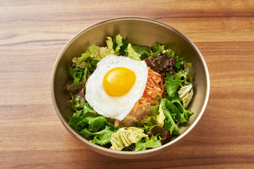 fried egg, with vegetable salad Is a healthy food Put in a Brass bowl placed on a wooden table.
