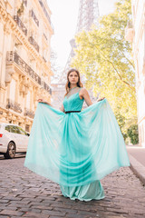 Fototapeta premium Beautiful young girl in a dress on the street with a view of the Eiffel tower