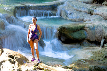 Traveler woman in swimsuit enjoy on stone at Erawan Waterfall