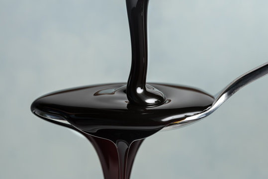 Close-up Of Molasses Syrup Pouring In Spoon Against Gray Background