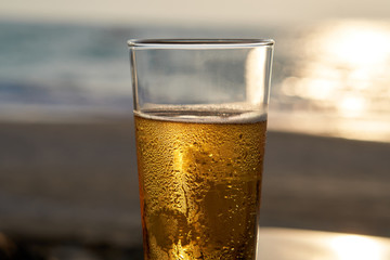 Cold beer in a glass at sunset, sea and beach in the background.
