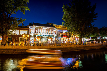 Beijing, China - July 31, 2019: Long exposure photograph of boats and pedestrians making their way around the bars, shops, and restaurants in the Houhai section of Beijing, China.