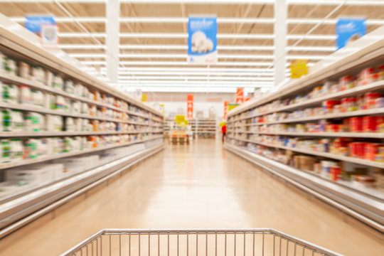 Blurred photos showcases shops on the background of a grocery cart. Long rows of racks with goods.