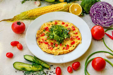 egg omelet with cherry tomatoes, cheese and arugula on a plate on the table with a white tablecloth