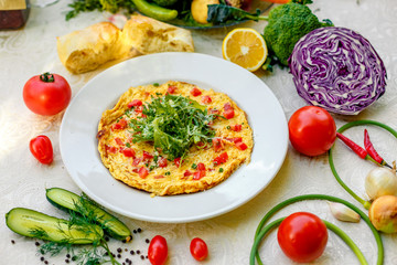 egg omelet with cherry tomatoes, cheese and arugula on a plate on the table with a white tablecloth