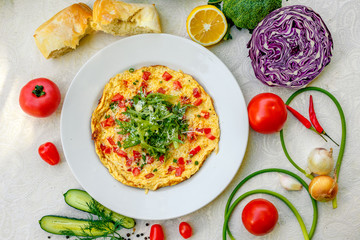 egg omelet with cherry tomatoes, cheese and arugula on a plate on the table with a white tablecloth