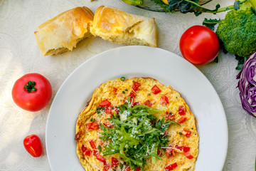 egg omelet with cherry tomatoes, cheese and arugula on a plate on the table with a white tablecloth