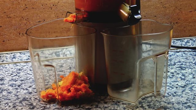 Fruit remains dropping into plastic can during process of making cold fresh fruit juice in juice maker.