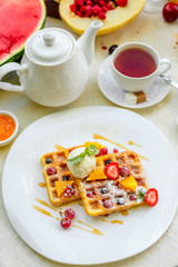 Belgian waffles with ice cream and fruits and berries on a white plate