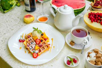 Belgian waffles with ice cream and fruits and berries on a white plate