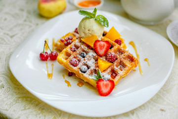 Belgian waffles with ice cream and fruits and berries on a white plate