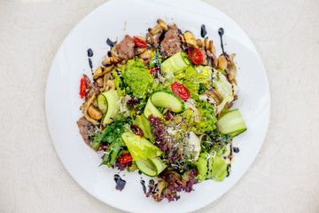 warm salad with meat, cucumber and vegetables on a white plate on the table