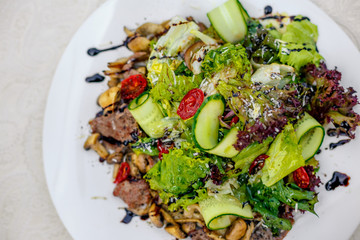 warm salad with meat, cucumber and vegetables on a white plate on the table