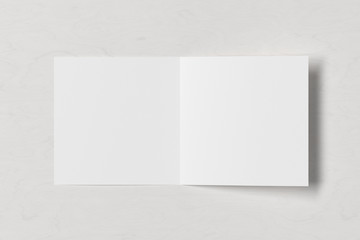 Blank square pages leaflet on white wooden background. Bi-fold or half-fold opened brochure isolated with clipping path. View directly above. 3d illustration