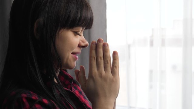 brunette girl makes a wish prayers bedtime religion concept. prayer woman mom indoors praying by bed front of window lifestyle