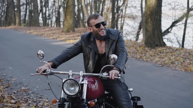 Portrait of biker behind a motorcycle smiling in park.