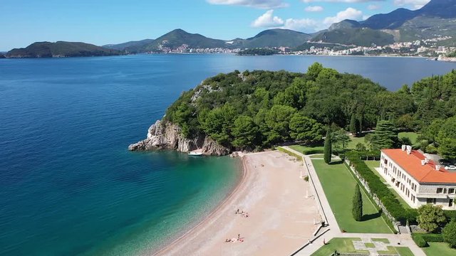Aerial shot over little peninsula toward town of Budva in Montenegro on a coast of Adriatic sea. Bright sunny day with blue sky and beautiful clouds.