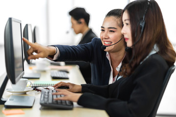 Group of happy asian smiling call center business operator customer support team phone services agen working and talking with headset on desktop computer at call center