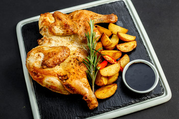 appetizing grilled chicken with homemade potatoes and sauce on a black tray