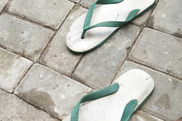 Warn out  green flip-flops  above paving concrete
