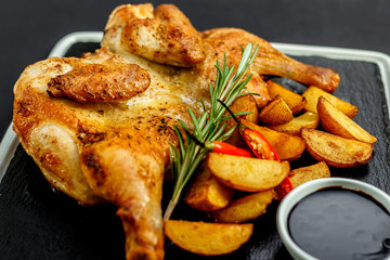 appetizing grilled chicken with homemade potatoes and sauce on a black tray