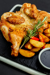 appetizing grilled chicken with homemade potatoes and sauce on a black tray