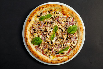 delicious Italian pizza with parmesan cheese, mushrooms, onions and basil on a black table