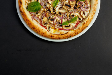 delicious Italian pizza with parmesan cheese, mushrooms, onions and basil on a black table
