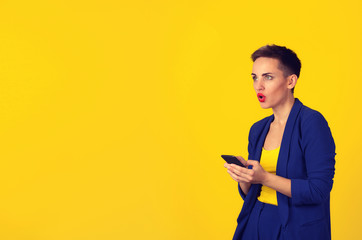 Closeup portrait shocked young girl looking up to the side phone in hands, she saw bad news or photos with disgusting emotion on her face isolated yellow background. Human emotion reaction expression