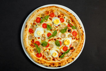 delicious Italian pizza with chicken sausages, eggs and basil on a black table
