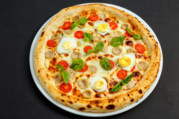 delicious Italian pizza with chicken sausages, eggs and basil on a black table