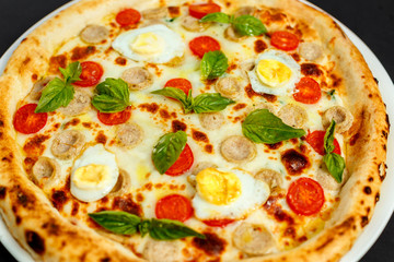 delicious Italian pizza with chicken sausages, eggs and basil on a black table