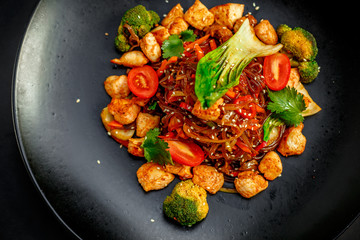 Thai cuisine, rice noodles with chicken, broccoli, tomatoes and greens