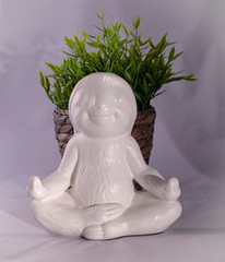 White smiling and calm looking sloth ornament sitting in the lotus meditating position with succulent plant and wicker basket