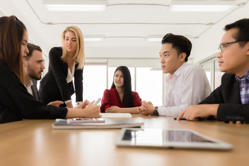 A group of office workers are sitting in a small meeting in the morning to get an assignment before starting work. On the table there are documents and tablets placed in the meeting room.