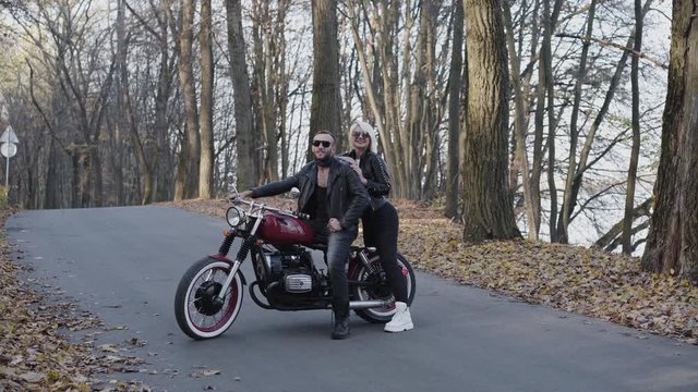 Portrait of happy female and male bikers behind motorcycle among park roadway