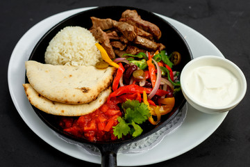 fried beef in a pan with rice, pita and vegetables